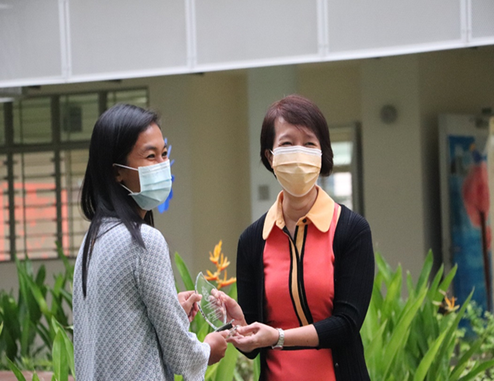 A teacher receiving the President’s Award for Teachers from Principal in the school courtyard.
